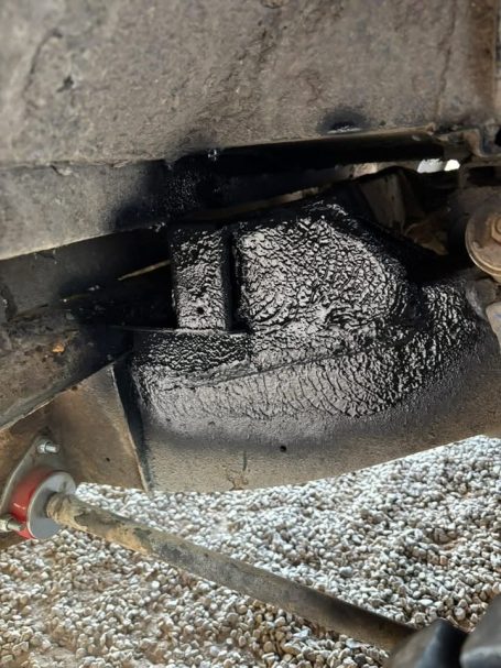 Close-up of a textured, dark surface underneath a vehicle component with gravel around it.