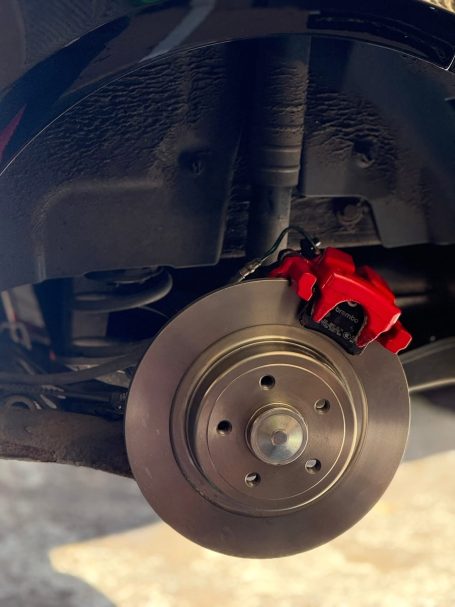 Close-up of a red brake caliper and disc on a vehicle's wheel assembly.