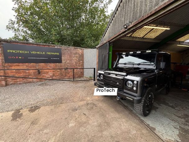 Black off-road vehicle parked in a garage with green and black signage in the background.